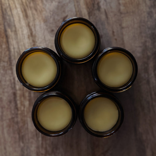 Five amber jars with a yellowish beard balm on a wooden surface