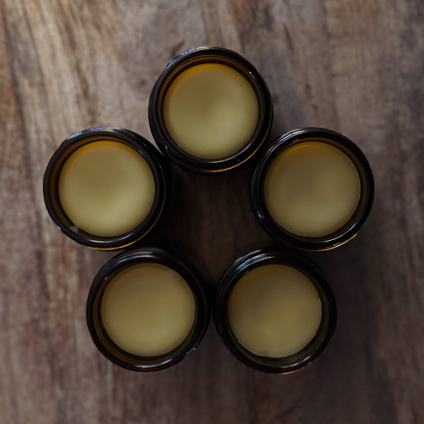 Five amber jars with a yellowish beard balm on a wooden surface
