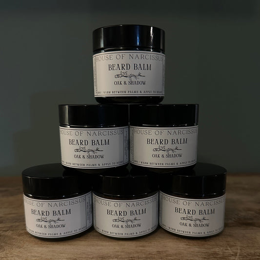 Stack of House of Narcissus beard balm jars on a wooden surface with a dark background